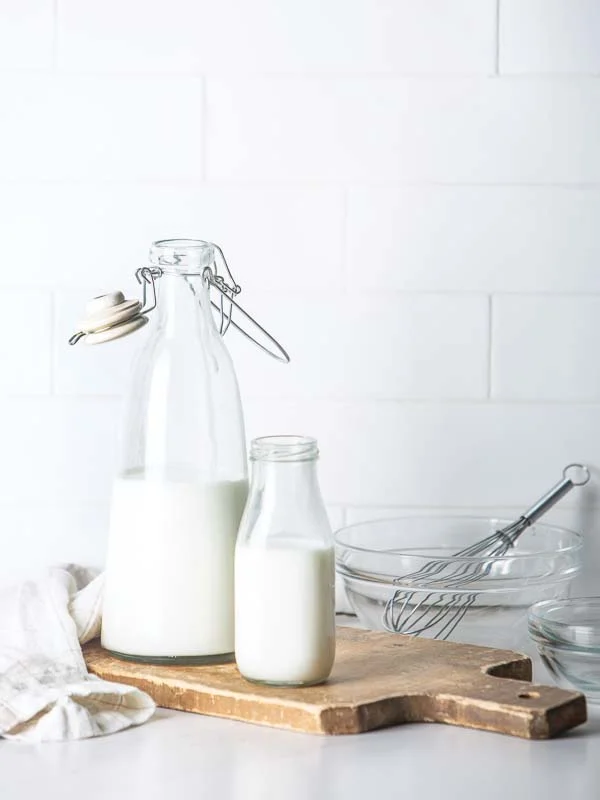 Buttermilk in glass carafes on wooden cutting board with mixing bowl and whisk on counter